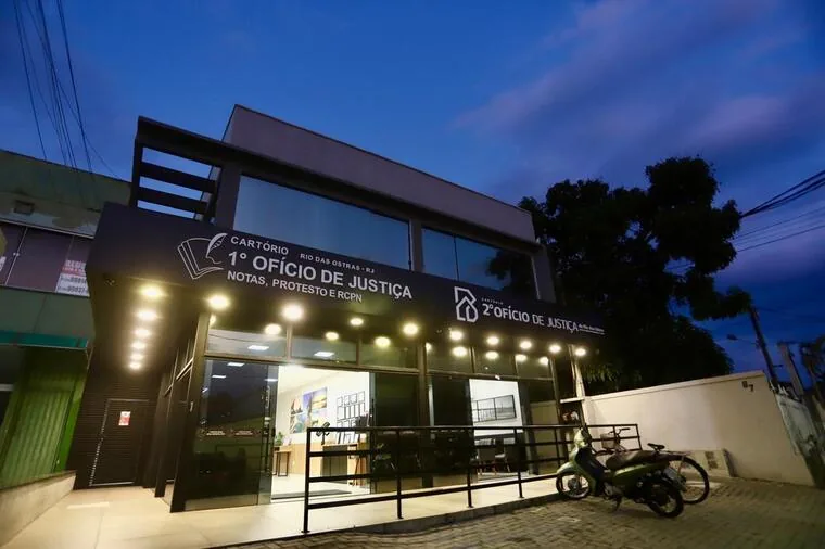 Fachada iluminada do Cartório 1º Ofício de Justiça ao anoitecer em Rio das Ostras
