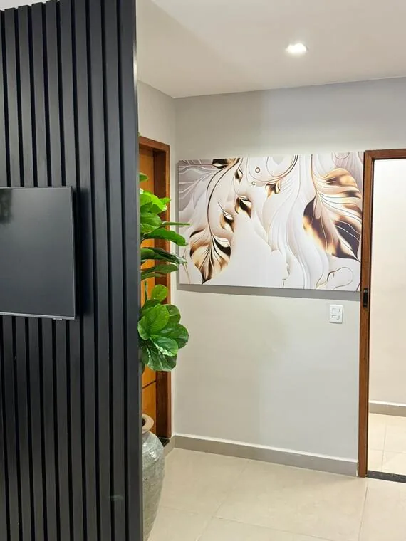 Corredor do cartório com painel ripado preto, televisão, planta e quadro abstrato dourado
