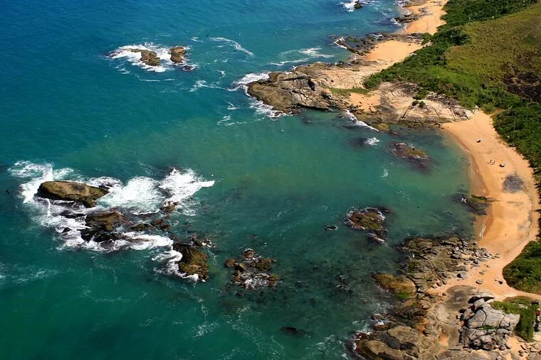Vista aérea da costa de Rio das Ostras com praia, pedras e mar esverdeado