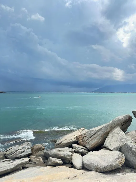 Costão de pedras claras e lancha ao longe no mar de Rio das Ostras