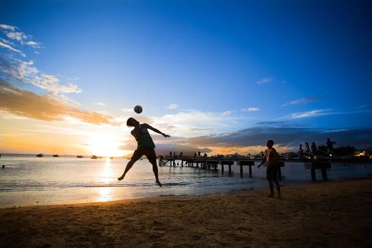 Jovens jogando futebol na areia ao pôr do sol em praia de Rio das Ostras