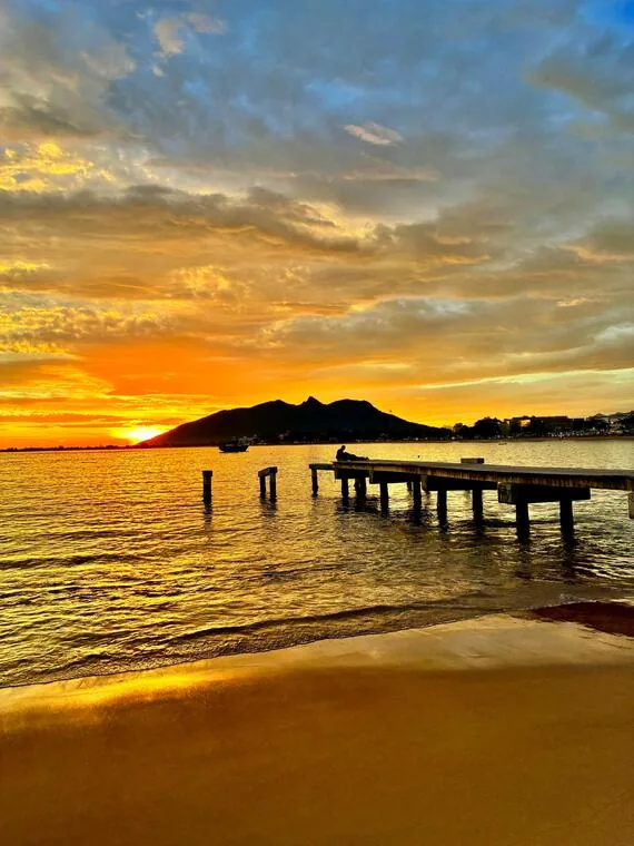 Pôr do sol dourado sobre o píer com montanha ao fundo em Rio das Ostras