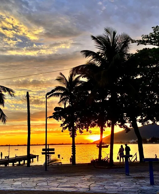 Coqueiros no calçadão da orla de Rio das Ostras durante o entardecer dourado