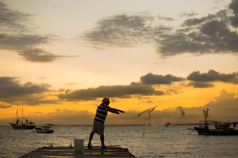 Pescador lançando a tarrafa do píer ao amanhecer dourado em Rio das Ostras