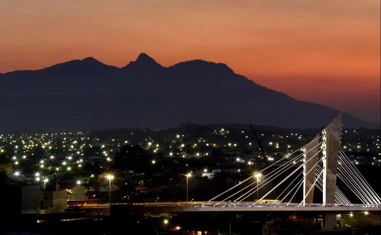 Ponte estaiada de Rio das Ostras iluminada ao entardecer com serra ao fundo
