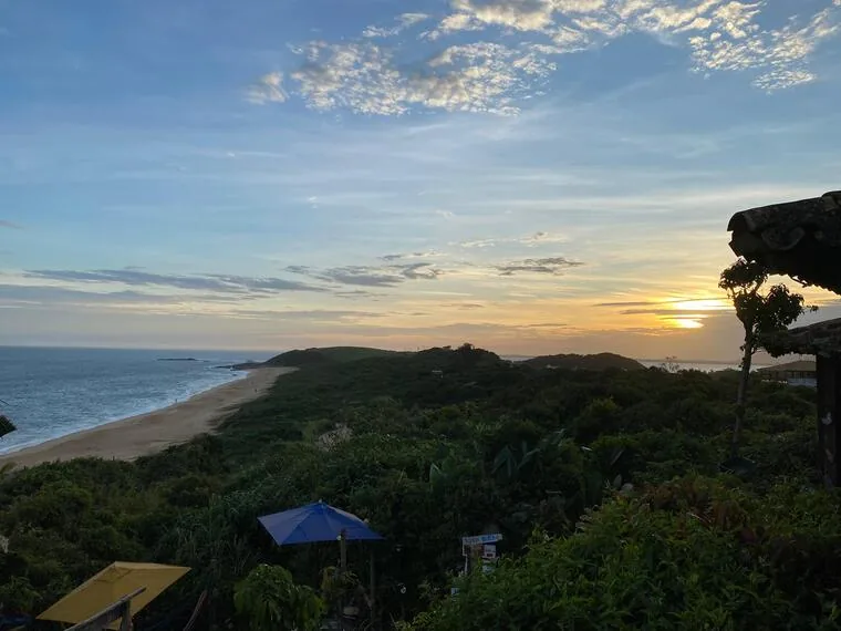 Vista do alto de praia extensa e vegetação em Rio das Ostras ao entardecer