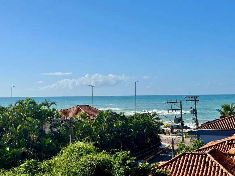 Mar azul visto entre telhados e vegetação da orla de Rio das Ostras