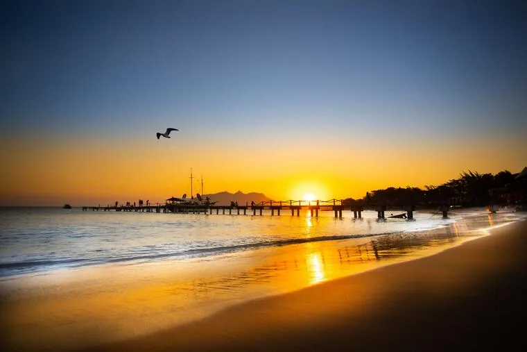 Pôr do sol na praia de Rio das Ostras com píer, barco e gaivota