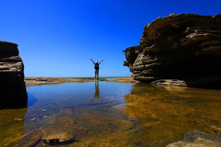 Visitante de braços abertos junto a piscina natural entre costões rochosos em Rio das Ostras