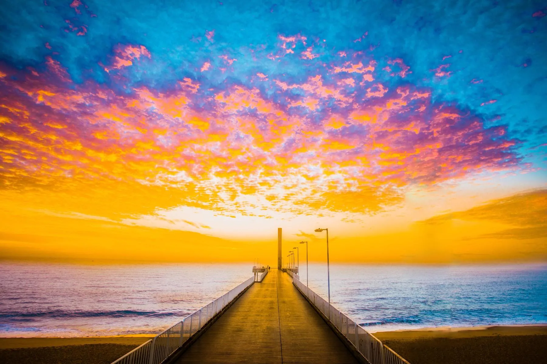 Píer avançando sobre o mar de Rio das Ostras sob um céu rosado no fim da tarde