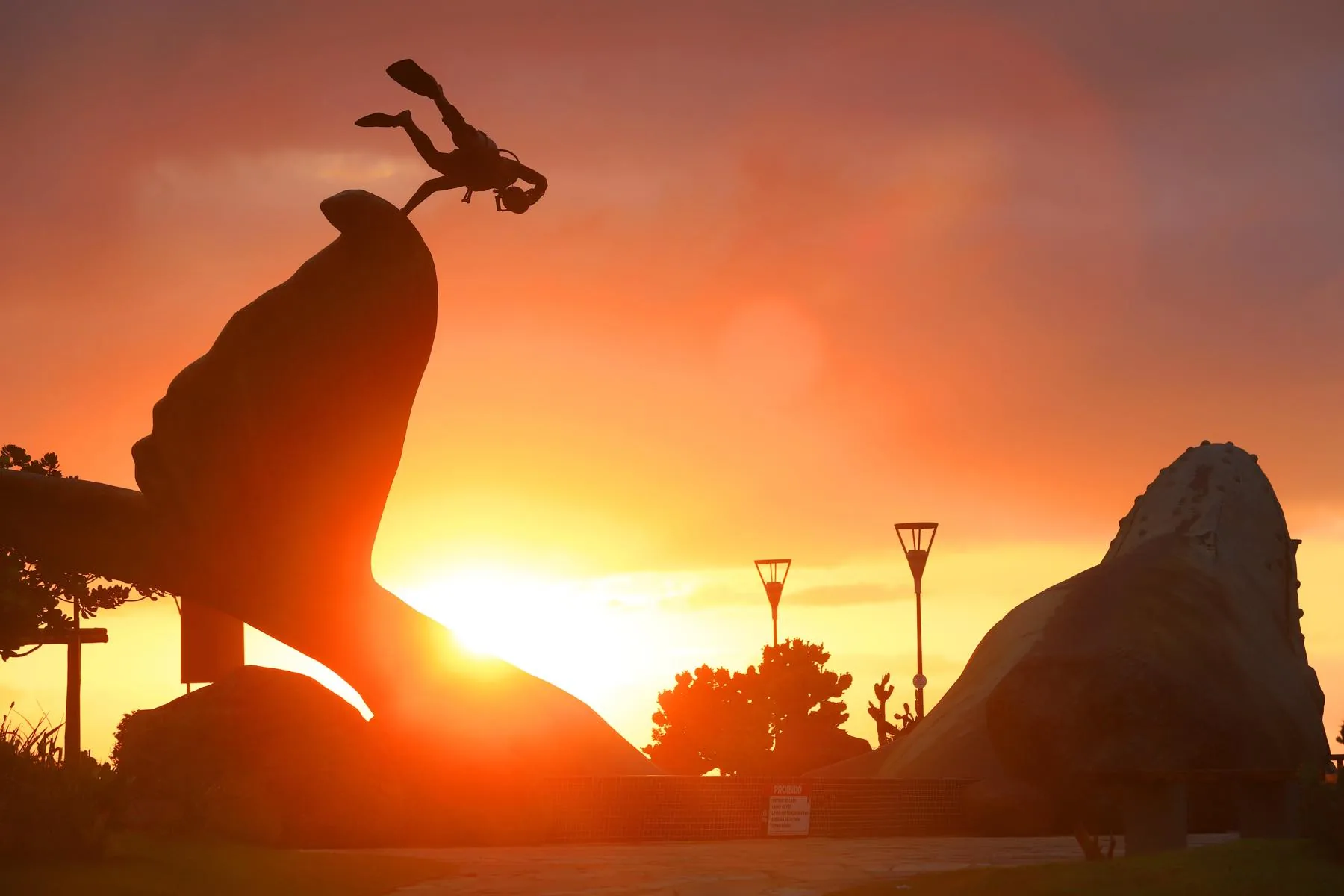 Silhueta do monumento da ostra recortada contra o céu alaranjado do pôr do sol